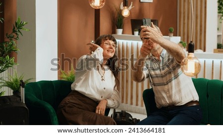 Elderly couple taking pictures at hotel, documenting all activities on international vacation together. Sweet husband and wife take photos on smartphone, making memories on retirement trip.