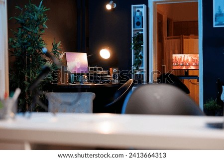 Work desk with computer and house plants in dimly lit empty home studio interior. Apartment illuminated by RGB lights with 3D rendered animations running on powerful PC monitors