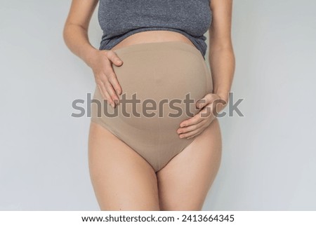 Pregnant bliss: Mom-to-be embraces her baby bump with a soft fabric bandage, providing gentle support. Maternity made comfortable Royalty-Free Stock Photo #2413664345