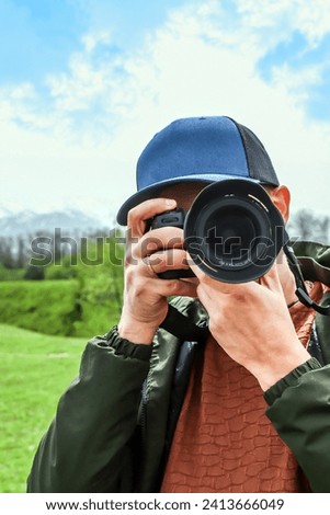 Photographer-naturalist.Photographer takes pictures with a camera standing on a green meadow with grazing horses against the backdrop of mountains