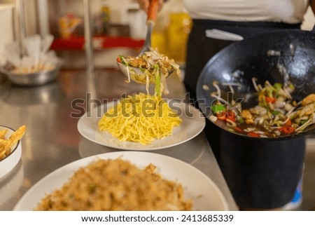 Cook plating vegetables with noddles in a counter of a restaurant kitchen