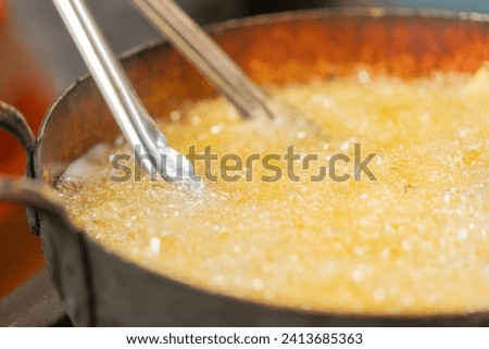Close-up and cropped photo of a cook using tweezers to remove potatoes in the frying pan