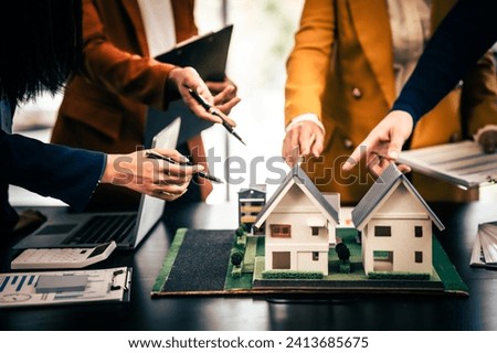 Asian real estate team engaged in a discussion, with two men and a woman focusing on a house model on a table, suggesting a planning or sales meeting. Royalty-Free Stock Photo #2413685675
