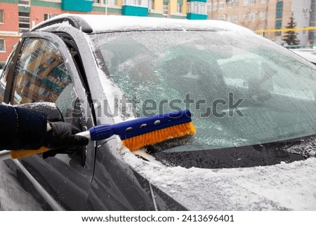 
cleaning the car glass with a broom from snow and ice in winter