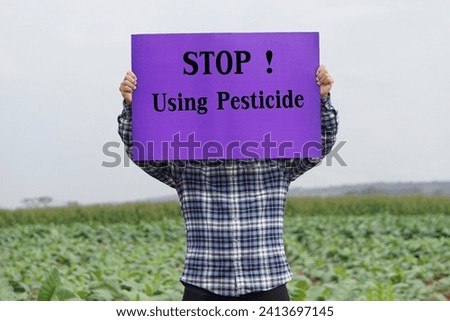Text Stop Using Pesticide on paper poster, held by farmer at garden. Concept, campaign for calling famers or gardeners to stop using pesticide or chemical with vegetables.                            