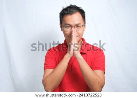 Close-up Portrait of young asian man staring with serious face wearing red shirt and glasses with both hand closed in front of his face. Isolated on white background.