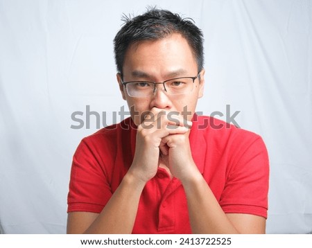 Close-up Portrait of young asian man staring with serious face wearing red shirt and glasses isolated on white background.
