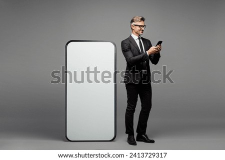 Full body fun adult employee business man corporate lawyer wear classic formal black suit shirt tie work in office big huge blank screen area using mobile cell phone isolated on plain grey background