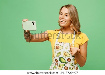 Young housewife housekeeper chef cook baker woman wear apron yellow t-shirt doing selfie shot on mobile cell phone get video call talk speak isolated on plain green background. Cooking food concept