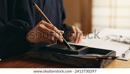 Hands, brush in ink for writing and Japanese calligraphy or ancient script for art and inkstone. Asian creativity, black paint and vintage tools, paintbrush and person with traditional stationery Royalty-Free Stock Photo #2413730297