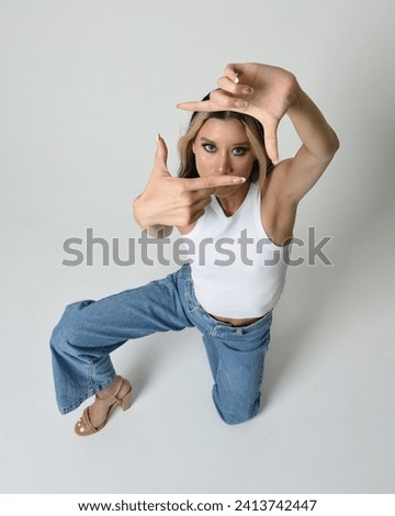 Full length portrait of brunette female asian model wearing casual clothes, white singlet shirt, denim jean pants. Sitting pose, high camera angle for perspective. Isolated on white studio background.