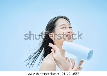 Young woman drying her hair with a hair dryer Royalty-Free Stock Photo #2413748553
