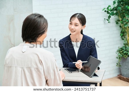 A woman in a suit explaining to a woman in plain clothes in the room Royalty-Free Stock Photo #2413751737