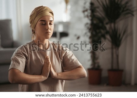 Young woman with cancer taking yoga and meditating in her apartment. Strong female patient calming her mind with easy exercise. Concept of mental health and cancer. Royalty-Free Stock Photo #2413755623