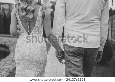 Bride and groom hold hands and walking on the street. Closeup. Details of wedding moments. Newlyweds together. Bride and groom walk outdoors. Back down view. Black and white photo. Couple hands.