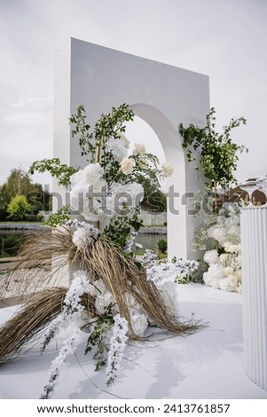 Wedding decor in banquet area. White arch for ceremony is decorated flowers and greens, greenery in backyard with lake view. Wedding decorations in luxury ceremony. Location for celebration on pier.