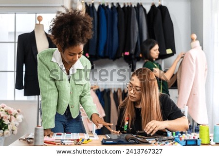 Portrait of young african american woman and asian woman fashion designer stylish sitting and working with color samples.Attractive two designer girl work with colorful fabrics at fashion studio