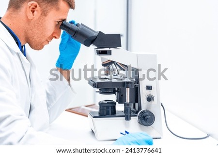Side close-up view of a male young doctor using microscope to analyze samples in a laboratory