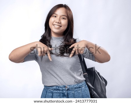 Portrait of an Indonesian Asian woman, wearing a gray dress, posing ready to go to campus with books and a bag, isolated against a white background.
