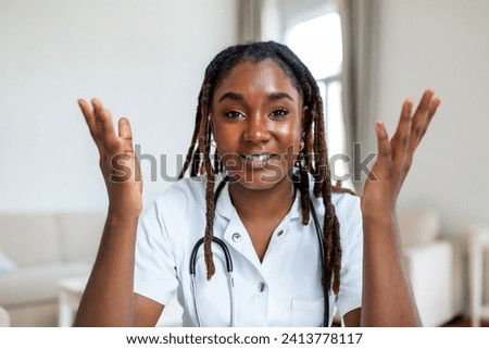 African woman doctor talking online with patient, making video call, looking at camera, young female wearing white uniform with stethoscope speaking, consulting and therapy concept