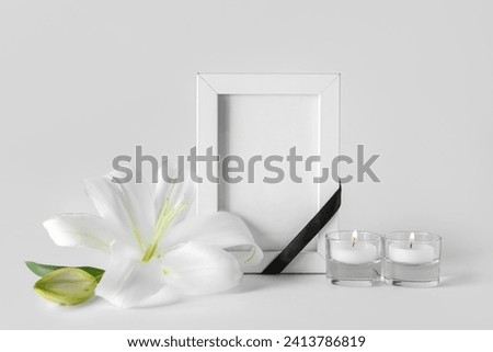 Blank funeral frame, burning candles and beautiful lily flowers on grey background