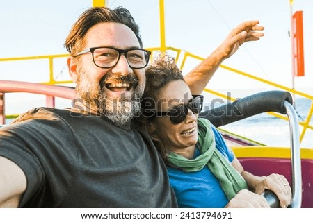 Adult couple have fun together on a roller coaster in amusement park taking selfie picture with the phone. People enjoying holiday lifestyle. Mature man and woman enjoy time outdoor leisure activity