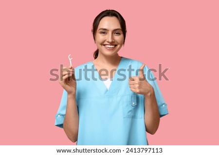 Young female dentist with floss toothpick showing thumb-up on pink background Royalty-Free Stock Photo #2413797113