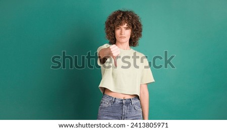 Adult woman with curly hair looking unhappy showing thumbs down gesture