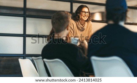 Group of colleagues engages in a dynamic discussion. A confident woman leads the team, presenting ideas to attentive businessmen and women. Their collaboration drives their tech startup's success. Royalty-Free Stock Photo #2413814025