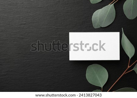 Blank business card and eucalyptus branches on black background, flat lay. Mockup for design