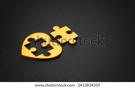 Gold heart with a detached puzzle piece, purposefully arranged on a black background. Love, relationships and Valentine's Day related concept. Royalty-Free Stock Photo #2413834359