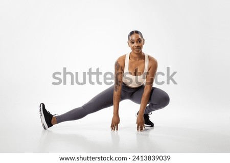 Athletic african american woman exercising stretching legs muscles in extended leg squat pose, having workout training over white studio background. Flexibility concept. Full length shot Royalty-Free Stock Photo #2413839039