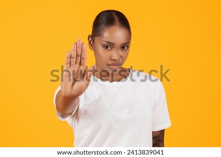 Determined angry african american young woman gesturing stop with hand, showing sign of protest and rejection on yellow studio background, closeup portrait. Stop abuse, discrimination and violence
