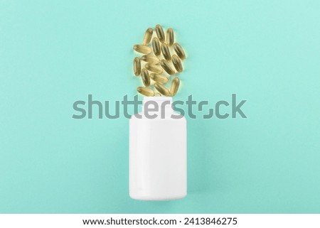 Bottle and vitamin capsules on turquoise background, top view