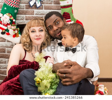 Happy family: black father, mom and baby boy by fireplace. Christmas and New Year