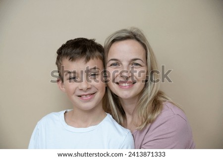 cool young teenager boy with white t-shirt posing together with his beautiful mother in front of brown background