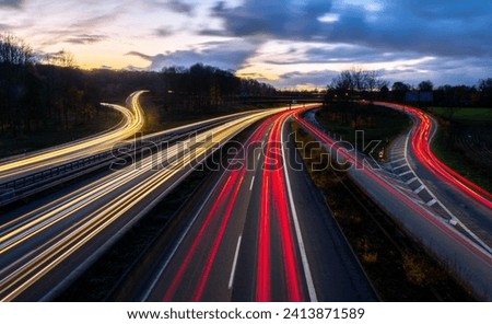 Autobahn crossing (A40 and A3) in Ruhr Basin Germany near Duisburg, Essen and Düsseldorf. Panoramic longtime exposure with red and white lights of passing cars at blue hour twilight after sunset. Royalty-Free Stock Photo #2413871589