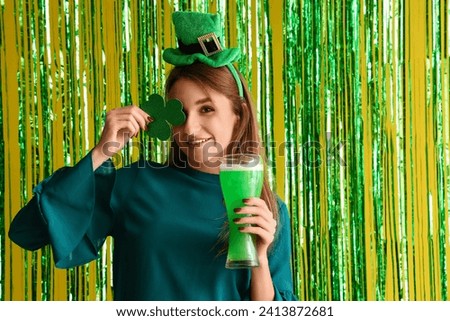 Young woman with beer and paper clover against tinsel on yellow background. St. Patrick's Day celebration