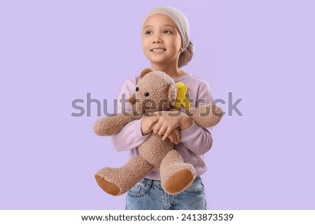 Cute little Asian girl after chemotherapy with yellow ribbon on lilac background. Childhood cancer awareness concept Royalty-Free Stock Photo #2413873539