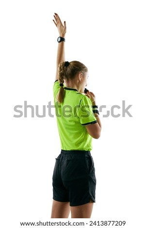 Back view. Young serious woman, soccer referee blowing a whistle and raising hand up as free kick symbol against white studio background. Concept of sport, competition, match, profession, football Royalty-Free Stock Photo #2413877209