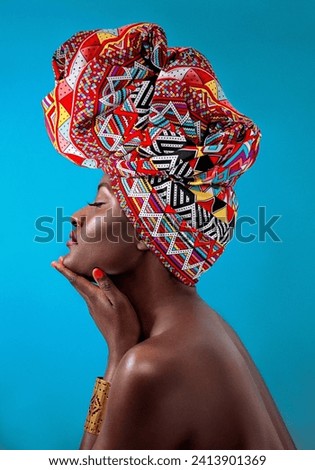 Beautiful young African woman wearing a Chevron pattern traditional headdress shaped like the African continent holding her chin with her eyes closed. Royalty-Free Stock Photo #2413901369