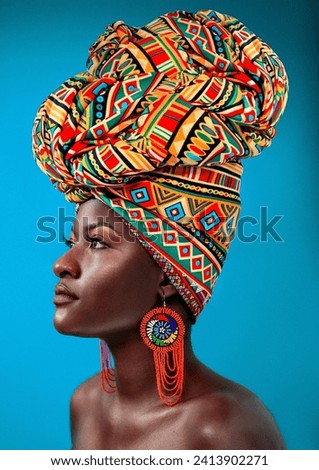 Beautiful young African woman wearing a Chevron pattern traditional headdress shaped like the African continent with beaded earrings facing sideways Royalty-Free Stock Photo #2413902271