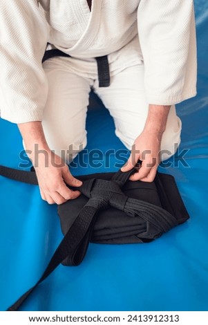Martial arts background. Aikidoka hands folding a black traditional hakama on a blue background. Royalty-Free Stock Photo #2413912313