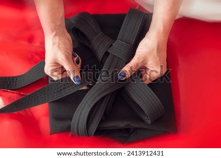 Martial arts background. Aikidoka hands folding a black traditional hakama on a red background. Royalty-Free Stock Photo #2413912431