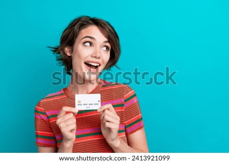 Photo of ecstatic woman dressed striped t-shirt holding debit card look at proposition empty space isolated on turquoise color background