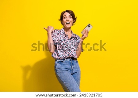 Photo of astonished attractive lady hold smart phone direct finger empty space isolated on yellow color background
