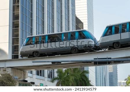 Public transportation in downtown Miami in Florida USA. Metrorail city train car on high railroad over street traffic between skyscraper buildings in modern American megapolis