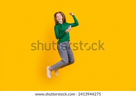 Full body length size photo of overjoyed teen girl jump up finally received credit ecard in phone isolated on yellow color background