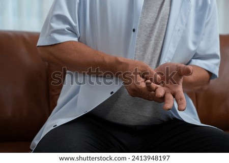 Elderly Asian male patients suffer from numbing pain in hands from rheumatoid arthritis. Senior men massage his hand with wrist pain. Concept of joint pain, rheumatoid arthritis, and hand problems.