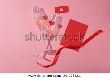 Two wine glasses in hologram color decorated with a red paper and a ribbon. Traditional gifts for Valentine include candy and flowers, particularly red roses, a symbol of beauty and love